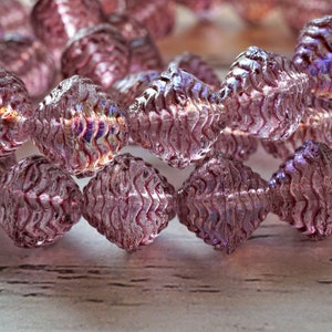 May include: A strand of iridescent purple glass beads with a textured, faceted design. The beads are strung together on a clear thread.