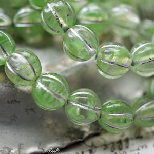 May include: Close-up of a strand of green, transparent beads with silver stripes. The beads are round and have a ribbed texture. The beads are strung together, creating a necklace or bracelet.