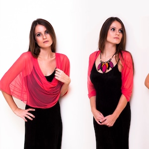 May include: Four women wearing different styles of a pink sheer shawl. The shawl is worn as a top, a scarf, and a wrap. The women are wearing black dresses.