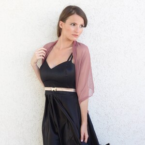 May include: A woman wearing a black dress with a gold belt and a dusty rose sheer shawl.