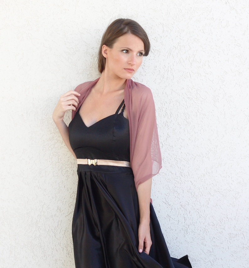 May include: A woman wearing a black dress with a gold belt and a dusty rose sheer shawl.