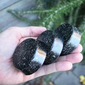 May include: Three round coasters with a black and white speckled design. The coasters are smooth and shiny.
