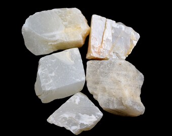 May include: Five white, opaque, natural mineral stones of various shapes and sizes. The stones have a slightly translucent quality and are arranged on a black background.