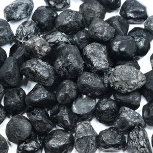 May include: A collection of black obsidian stones, each with a unique shape and texture. The stones are smooth and polished, with a deep black color.