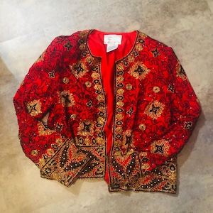 May include: A red jacket with intricate gold and black beadwork. The jacket features a round neckline and long sleeves. The design includes floral and geometric patterns, with a red satin lining. The jacket is a vintage piece.