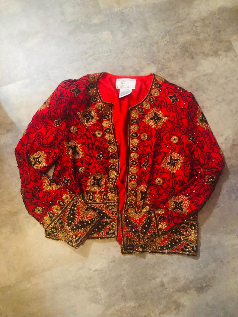 May include: A red jacket with intricate gold and black beadwork. The jacket features a round neckline and long sleeves. The design includes floral and geometric patterns, with a red satin lining. The jacket is a vintage piece.
