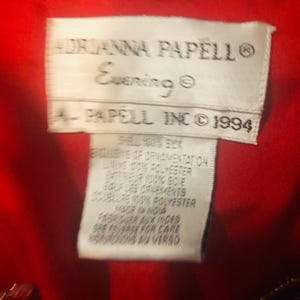 May include: A close-up of a tag from an Adrianna Papell Evening garment. The tag is white with black text, including the brand name, "Evening," and "A. Papell Inc &copy; 1994." The tag also lists fabric content and care instructions.