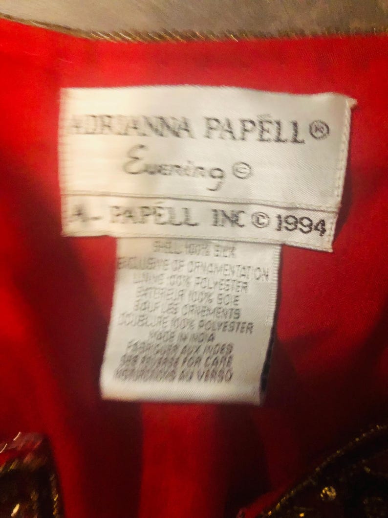May include: A close-up of a tag from an Adrianna Papell Evening garment. The tag is white with black text, including the brand name, "Evening," and "A. Papell Inc &copy; 1994." The tag also lists fabric content and care instructions.