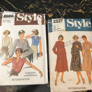 May include: Two vintage sewing pattern packets. The left packet, labeled "2986," features illustrations of women's blouses and a jacket. The right packet, "2537," showcases dresses. Both packets are from "Style" and include size and pattern details.