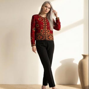May include: A red jacket with intricate gold and black embroidery. The jacket has long sleeves and a round neckline. Paired with black trousers and heels. The outfit is suitable for formal occasions.
