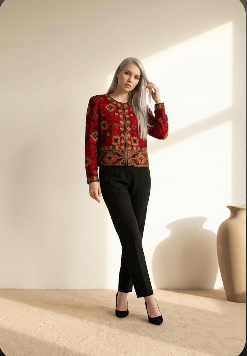 May include: A red jacket with intricate gold and black embroidery. The jacket has long sleeves and a round neckline. Paired with black trousers and heels. The outfit is suitable for formal occasions.