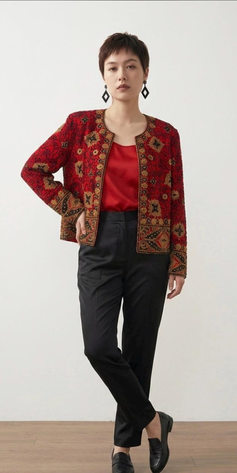 May include: A red beaded jacket with gold and black floral embroidery. The jacket is worn over a red top and paired with black pants and loafers. The outfit is a stylish ensemble.
