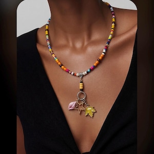 May include: A vibrant beaded necklace with a pendant. The pendant includes a pink leaf, a gold star, and a yellow leaf. The necklace is made of small beads in various colours, including yellow, orange, pink, blue, and white.