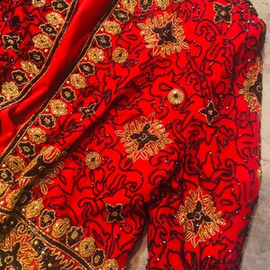 May include: A red jacket with intricate gold and black beadwork. The jacket features floral and scroll patterns, with a V-neckline and long sleeves. The embellishments create a textured, ornate design.