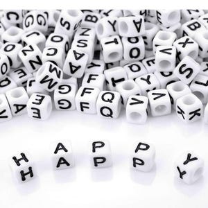 Könnte beinhalten: Weiße Buchstabenperlen mit schwarzen Buchstaben, die auf einer weißen Oberfläche verstreut sind. Das Wort "HAPPY" ist mit den Perlen im Vordergrund geschrieben. Diese Perlen sind ideal für die Schmuckherstellung und das Basteln.
