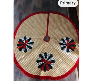 May include: A gold quilted Christmas tree skirt with a red border and three decorative floral accents. The accents feature red, green, and white fabric. A red fabric loop is at the center.