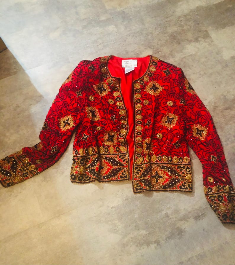 May include: A red jacket with intricate gold and black embroidery. The jacket features a round neckline and long sleeves. The embroidery includes floral and geometric patterns. The jacket is open in the front, revealing a red lining.