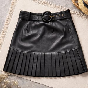 May include: A black leather skirt with a pleated hem and a belt with a large, round buckle. The skirt has a tailored design and a classic, versatile style. The belt has a series of small gold-colored rivets.