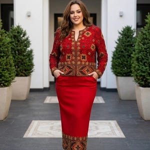 May include: A red skirt suit with an embroidered jacket. The jacket features intricate gold and brown patterns on a red background. The skirt is a solid red color. The outfit is worn with black sandals.
