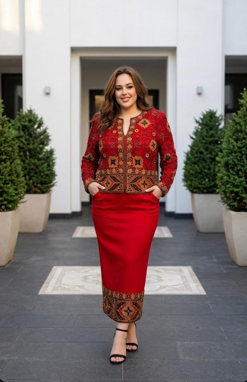 May include: A red skirt suit with an embroidered jacket. The jacket features intricate gold and brown patterns on a red background. The skirt is a solid red color. The outfit is worn with black sandals.