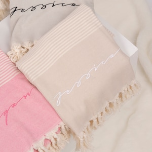 May include: Two beige and pink striped towels with fringe edges. The towels have the name "Jessica" embroidered on them in black and white thread.