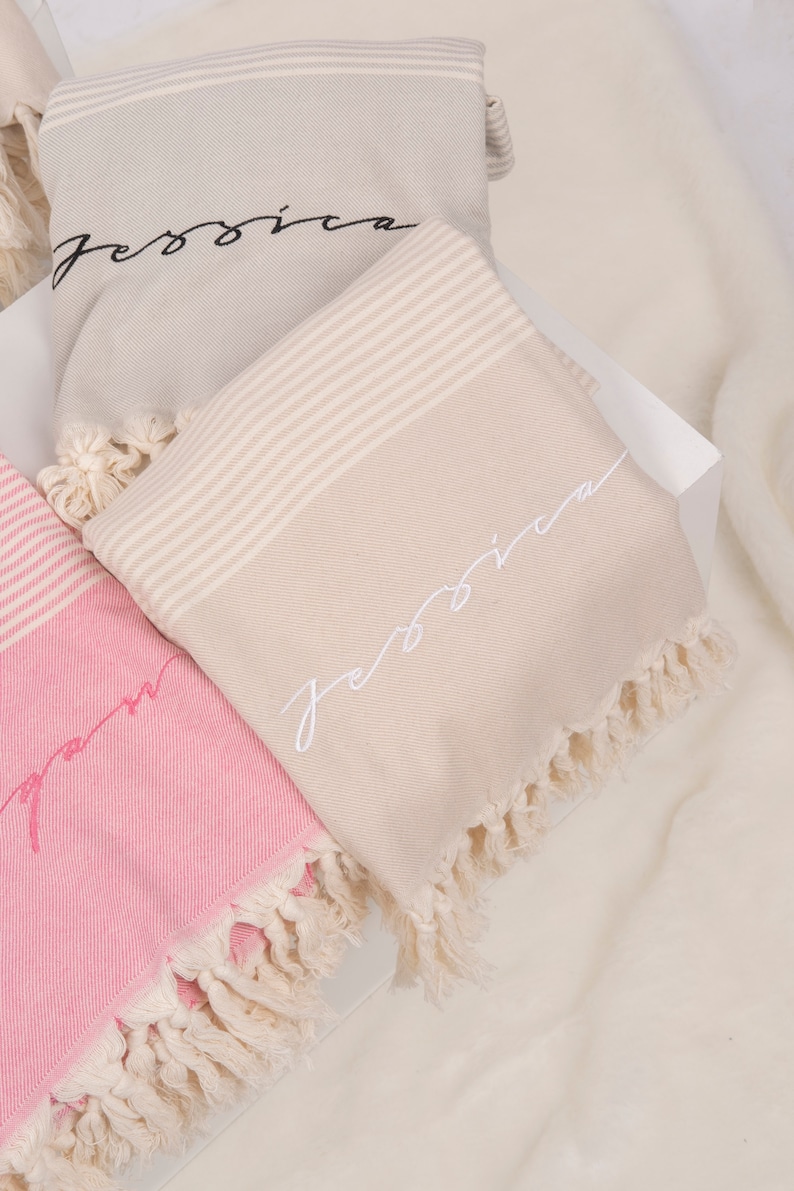 May include: Two beige and pink striped towels with fringe edges. The towels have the name "Jessica" embroidered on them in black and white thread.