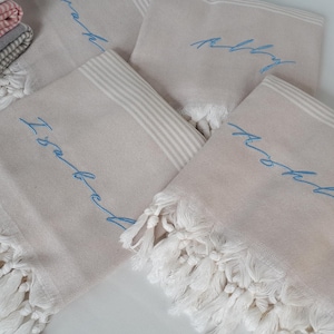 May include: Four beige towels with white fringe. The towels have blue embroidery that reads "I said yes", "happily", "happily", and "I said yes".