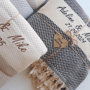 Puede incluir: Varias mantas tejidas plegadas con bordados personalizados. Una manta tiene un patrón en blanco y negro con una etiqueta en forma de corazón que dice "Happy Birthday". Otras mantas son beige y grises con nombres y fechas.