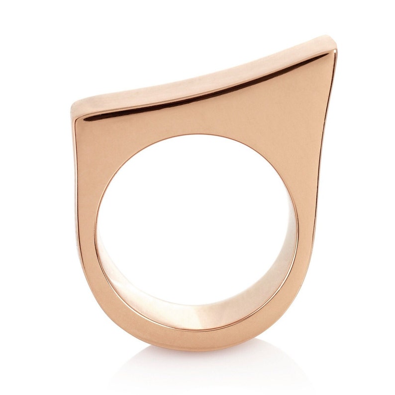 May include: A rose gold ring with a unique, angular design. The ring is made of a smooth, polished metal and has a simple, modern aesthetic.