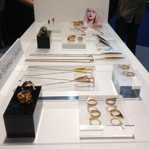 May include: A display of gold and rose gold jewelry on a white surface. The jewelry includes necklaces, rings, and earrings. The jewelry is arranged in a geometric pattern. The text "The Rebellion Collection" is visible in the lower left corner of the image.
