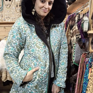 Peut inclure: Longue veste matelassée à motifs floraux bleus, verts et blancs. La veste a une doublure à capuche noire et une fermeture éclair sur toute la longueur. Coupe ample, idéale pour les températures fraîches.