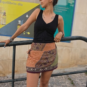 Peut inclure: Un haut noir sans manches à col en V avec un centre froncé et une mini-jupe patchwork multicolore ornée de motifs floraux, de tons orange et vert terreux, et de lacets latéraux avec un ourlet violet foncé et des surpiqûres blanches.