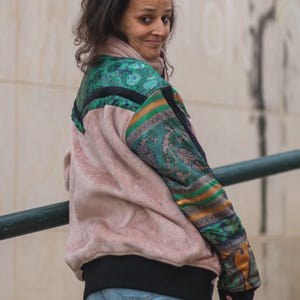 Peut inclure: Une veste à manches longues avec un corps en fausse fourrure rose pâle et un ourlet côtelé noir. Les manches et le panneau supérieur du dos présentent un motif cachemire vert, doré et bleu foncé avec des fleurs et des rayures horizontales.