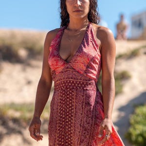 Peut inclure: Une robe longue sans manches à encolure américaine, ornée d'un motif cachemire rouge et orange vif. Le vêtement présente un décolleté en V profond, un corsage ajusté avec une taille marquée et une jupe fluide descendant jusqu'au sol.