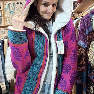 Peut inclure: Manteau à capuche rose vif avec un motif floral turquoise et orange. L'intérieur est doublé d'une douce fourrure blanche et se ferme par une fermeture éclair. Les manches et la capuche sont doublées du même tissu.