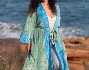 May include: A long, flowing robe with a floral pattern in shades of green and blue. The robe has a contrasting blue trim and a matching belt. The garment is worn over a white top and blue jeans.