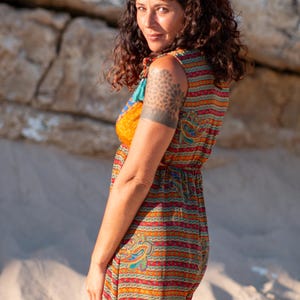 Peut inclure: Une robe sans manches présentant un motif multicolore vibrant avec des rayures horizontales dans des tons orange, rouge, vert et bleu, accentuée par des motifs cachemire complexes sur tout le tissu et une taille froncée.