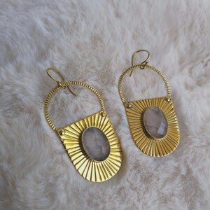 Peut inclure: Une paire de boucles d'oreilles dorées avec un sommet en fil circulaire et une base en éventail aux lignes rayonnantes. Chaque boucle est centrée par une pierre ovale à facettes rose pâle et possède un crochet incurvé.
