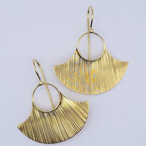 Peut inclure: Une paire de boucles d'oreilles dorées composées d'un pendentif en forme d'éventail suspendu à un anneau circulaire. La partie en éventail présente une fine texture gravée verticale qui capte la lumière, avec un crochet simple.