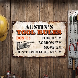 Peut inclure: Une plaque métallique rectangulaire avec un fond blanc vieilli et un texte noir et orange indiquant AUSTIN'S TOOL RULES. La plaque présente une illustration en noir et blanc d'un doigt pointé et énumère quatre règles : DON'T TOUCH 'EM, BORROW 'EM, MOVE 'EM, DON'T EVEN LOOK AT 'EM.