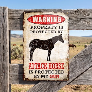 May include: A rectangular metal sign with a distressed, weathered finish. It features a red oval at the top with the word WARNING. Below, it reads PROPERTY IS PROTECTED BY, followed by a black horse silhouette, and ATTACK HORSE IS PROTECTED BY MY GUN.