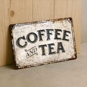 Vintage-style metal sign reading 'COFFEE AND TEA' with distressed white background and rusted edges