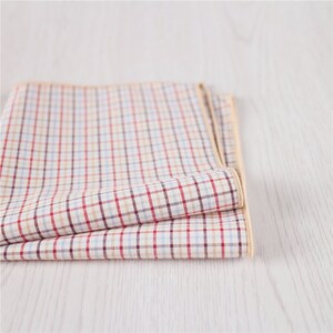 May include: A folded checkered handkerchief with a cream, red, and blue pattern and a cream border.