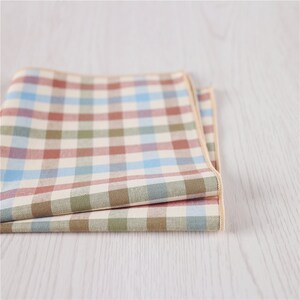 May include: A folded checkered fabric handkerchief in shades of brown, green, blue, and white with a cream border.