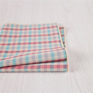 May include: A folded checkered fabric napkin in shades of red, blue, and gray with a cream background. The napkin has a light brown border.