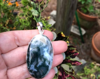 May include: A silver pendant featuring a large oval-shaped green and white agate stone. The stone has a swirling pattern of green, white, and gray.