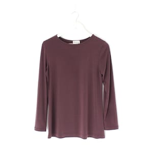 May include: A long-sleeved, burgundy-colored shirt hangs from a white hanger against a white background. The shirt has a crew neck and a simple, classic design. The fabric appears to be soft and comfortable, suitable for casual wear.