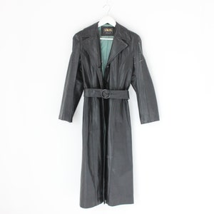 Puede incluir: Un abrigo largo de cuero negro con cinturón y forro verde. El abrigo tiene cuello y mangas largas.