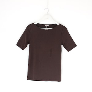 May include: A short-sleeved, dark brown t-shirt hangs from a white hanger against a white background. The shirt has a crew neck and a simple, classic design, suitable for casual wear.