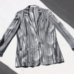 Peut inclure: Un blazer à manches longues avec un motif géométrique en chevrons noir et blanc. Le vêtement comprend un revers cranté, une fermeture simple boutonnage avec deux boutons visibles, une poche poitrine et deux poches plaquées sur le devant.